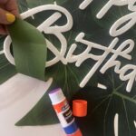 2. GLUE PALM LEAVES: Using a glue stick, carefully lift all the artificial palm leaves sections and glue them down onto the white posterboard.